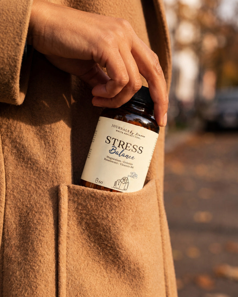 Stress Balance wird in die Tasche eines Kamelmantels gesteckt, herbstliche Straße im Hintergrund