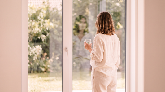 Woman looking out a bright window holding a glass of water, loving someone you cannot talk about