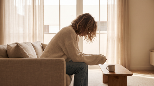 Woman sitting on the edge of a sofa with lowered head in morning light, loving someone in secret is exhausting