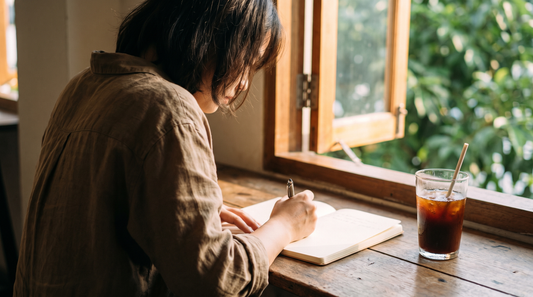 Woman writing by hand in a journal at a sunlit window on a summer morning, what is emotional clarity journaling