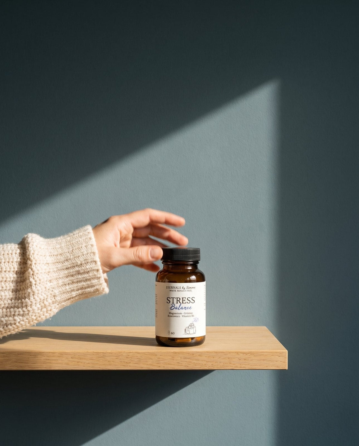 Braune Glasflasche Stress Balance mit Etikett Magnesium, Grüntee, Rosenwurz und Vitamin B6 auf einem Eichenregal, eine Hand greift danach
