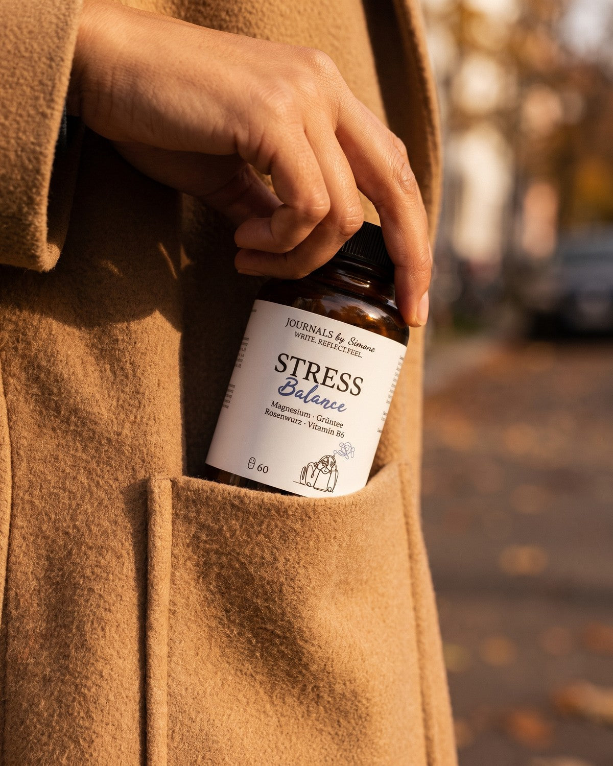 Eine Hand steckt Stress Balance in die Tasche eines Kamelmantels, im Herbstlicht auf der Strasse